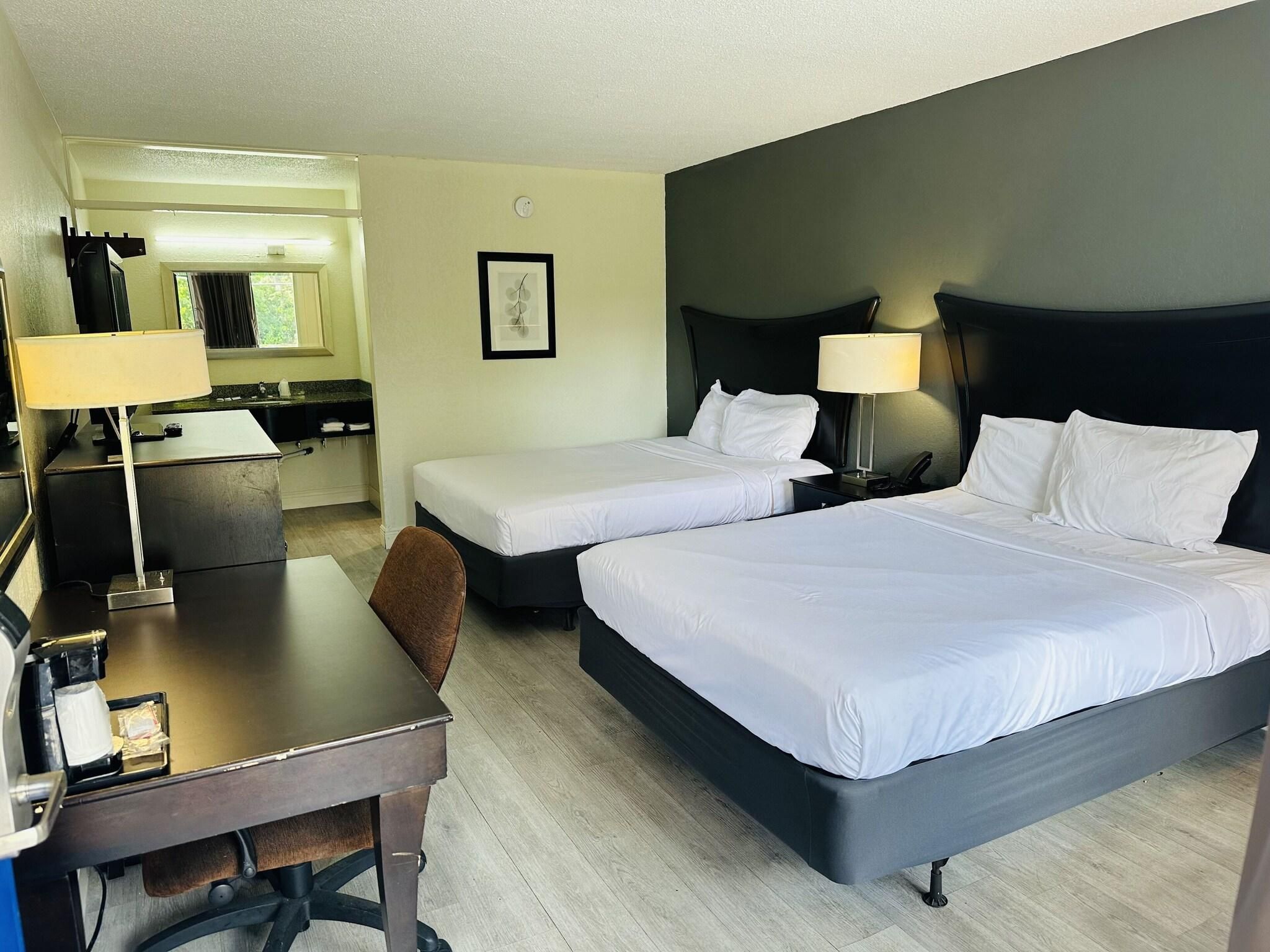 A hotel room with two beds, a desk, a chair, a lamp, and a small table.