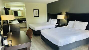 A hotel room with two beds, a desk, a chair, a lamp, and a small table.
