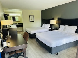 Habitación de hotel con dos camas, un escritorio, una silla, una lámpara y una mesita.
