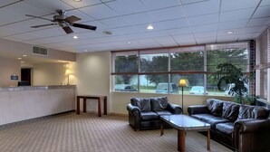 A hotel lobby with a reception desk, a ceiling fan, a coffee table, a sofa, and large windows with blinds. - Rodeway Inn Silver Springs (Silver Springs)