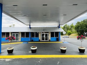 Una gasolinera con fachada azul y blanca, un acceso cubierto y plantas en macetas al frente.