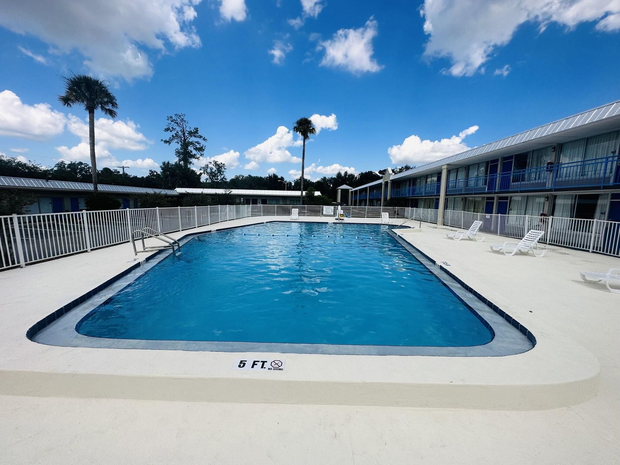 Ein rechteckiger Pool mit einer 1,5 Meter Tiefenmarkierung, umgeben von einem weißen Zaun und Liegestühlen.
