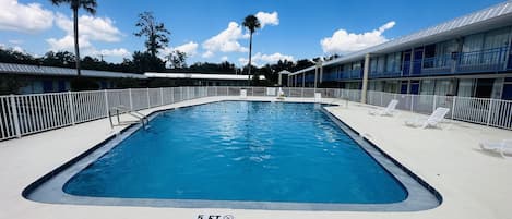 A rectangular swimming pool with a 5 ft depth marker, surrounded by a white fence and lounge chairs.