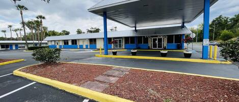 Una estación de servicio con un edificio azul y blanco, un área de estacionamiento techada y un estacionamiento con bordillos amarillos.