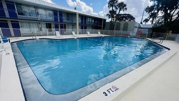 Uma piscina retangular com um aviso de 3 FT, proibido mergulhar, rodeada por um deck branco e um edifício com varandas azuis.