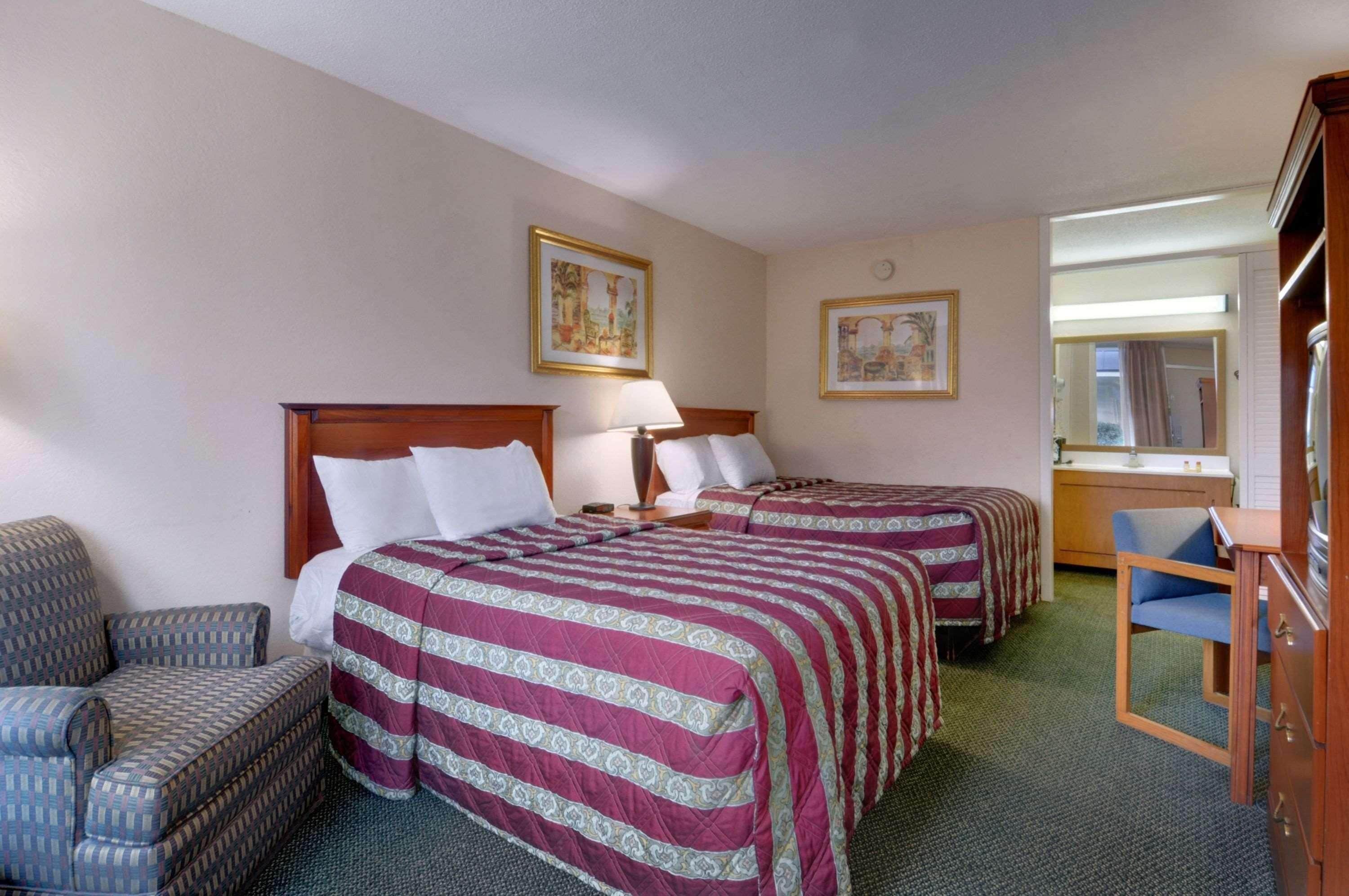 A hotel room with two beds, a chair, a desk, and a mirror.