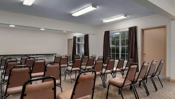 Ein Konferenzraum mit Reihen von Stühlen, einer Projektionsleinwand und einem großen Fenster mit Vorhängen.