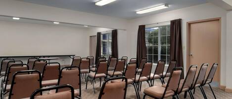 A conference room with rows of chairs, a projector screen, and a large window with curtains.