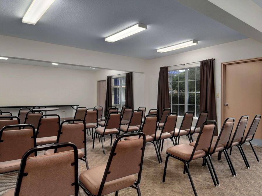 A conference room with rows of chairs, a projector screen, and a large window with curtains.