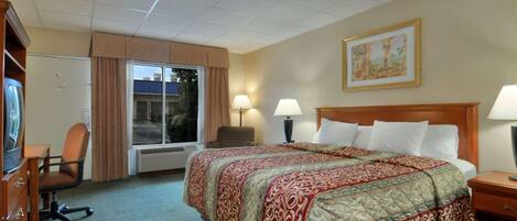 A hotel room with a large bed, two bedside lamps, a desk with a chair, a window with curtains, and a framed picture on the wall.