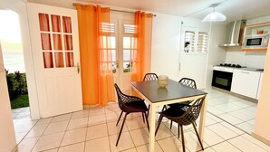 Un coin repas avec une table et des chaises, une cuisine équipée d’un four à micro-ondes et d’une cuisinière, et une porte avec des rideaux orange.