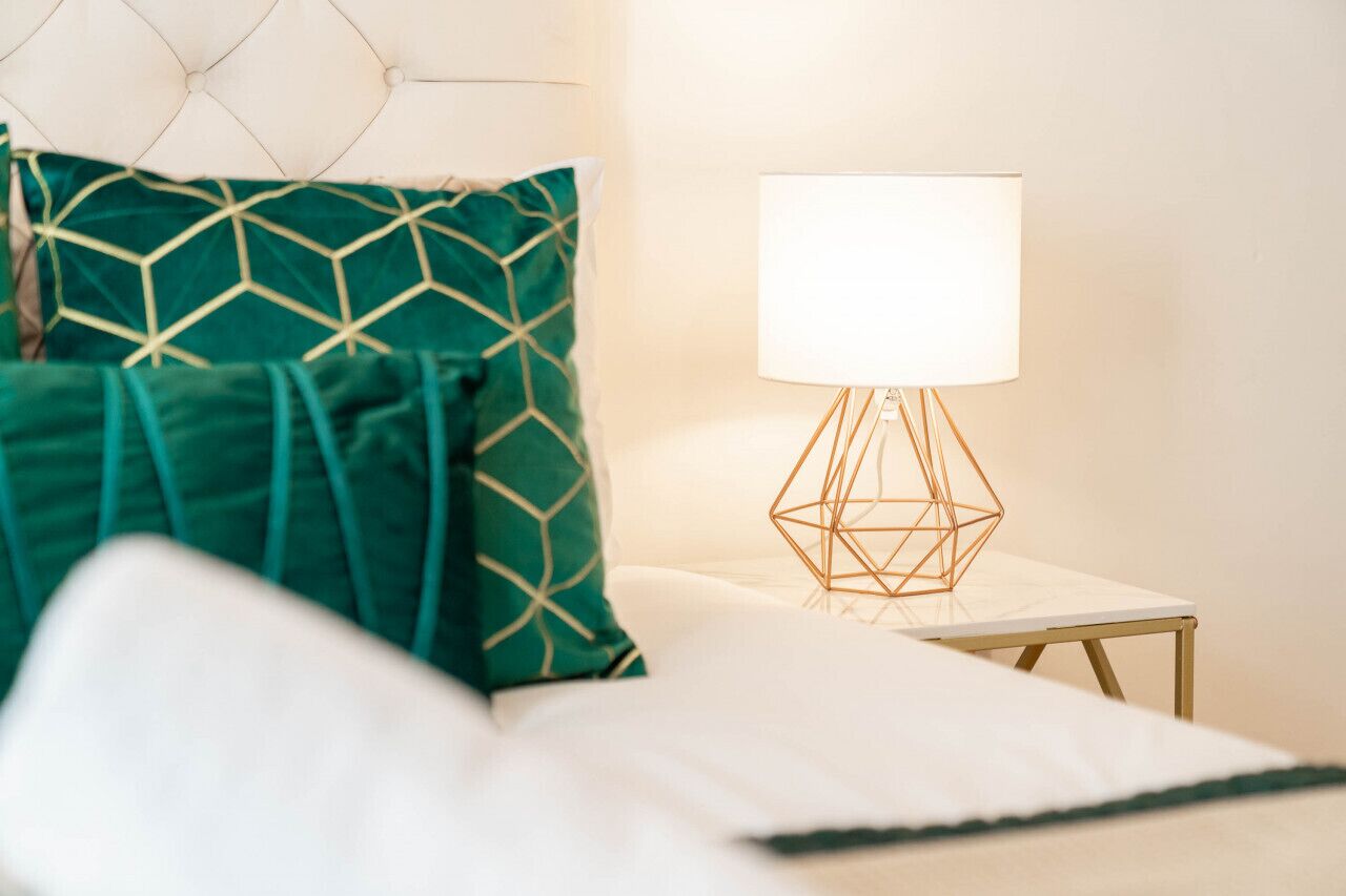 A neatly made bed with green and white bedding, a geometric-patterned pillow, and a bedside table with a white lamp.