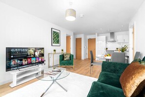 A modern living room with a flat-screen TV, a glass coffee table, a green sofa, and a dining area with a white table and chairs. - Birmingham City Centre - 2 Bed - Secure Parking
 (West Midlands)