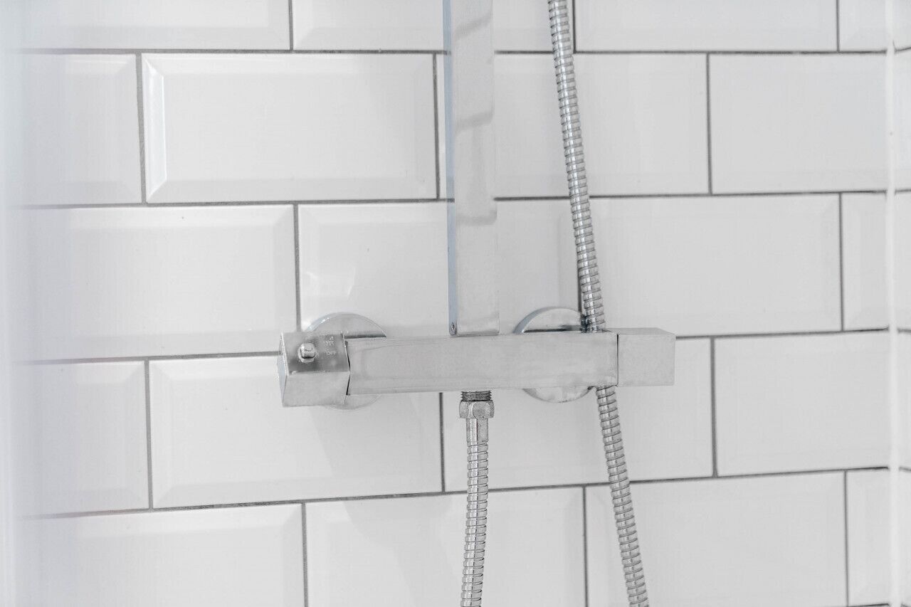 Une douche avec un robinet et un flexible chromés, le tout installé sur un mur carrelé.
