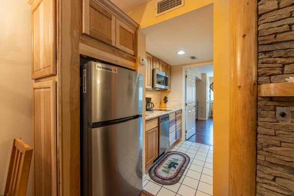 Una cocina con armarios de madera, un refrigerador de acero inoxidable, un microondas y piso de baldosas.