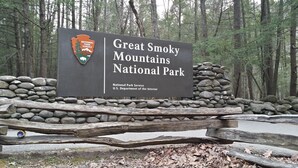 A sign for Great Smoky Mountains National Park with a stone wall and wooden fence.