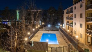A nighttime view of a hotel with a swimming pool, surrounded by trees and illuminated by streetlights.
