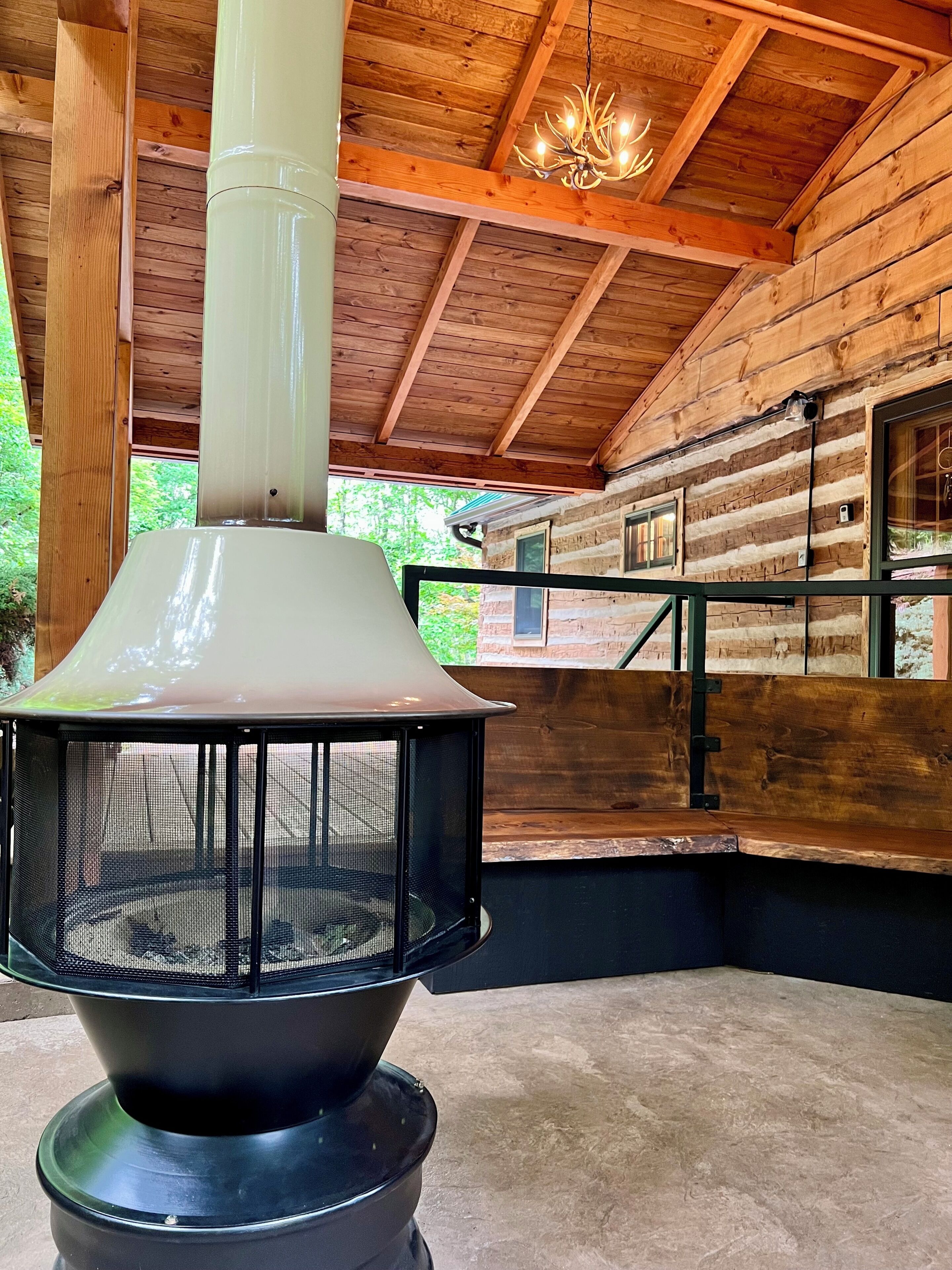 L’intérieur d’une cabane en rondins, avec un poêle à bois, un lustre et une vue sur la forêt environnante.