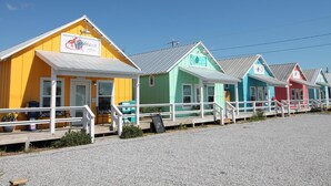 Une rangée de charmantes maisons de plage aux couleurs vives, dotées de balustrades blanches, et une route de gravier devant.
