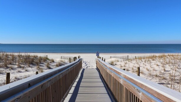 Une promenade en bois qui mène à une plage, avec un ciel bleu dégagé.