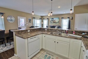 Cocina con gabinetes blancos, encimeras de granito, pileta doble e iluminación colgante.