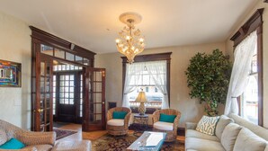 Un salón amplio con una araña, muebles de mimbre, un sofá blanco y una planta grande.