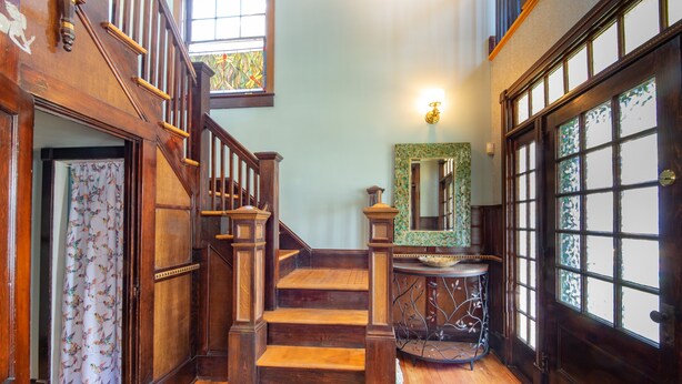 Una escalera de madera con barandilla, un espejo y una puerta con paneles de vidrio.
