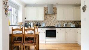 Una cocina con armarios blancos, estufa, horno y un comedor con mesa y sillas de madera.