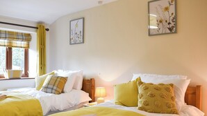 A room with two beds, each with yellow bedding and pillows, a window with a plaid curtain, and a wall-mounted picture frame. - 3 bedroom accommodation in Sockbridge, near Penrith (Sockbridge, near Penrith)