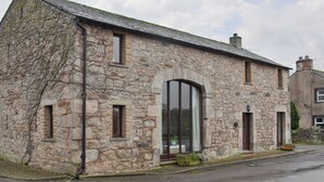 A stone building with a sloped roof, large arched windows, and a chimney. - 3 bedroom accommodation in Sockbridge, near Penrith (Sockbridge, near Penrith)
