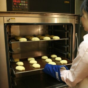 A person baking in a commercial oven with multiple trays of dough.
