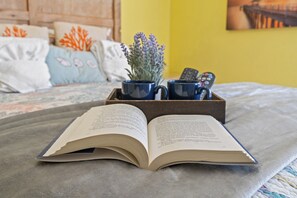 Un livre ouvert sur un lit, avec un plateau contenant deux tasses et une télécommande.