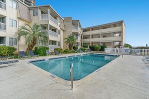 Une piscine entourée de bâtiments à plusieurs étages dotés de balcons, avec des chaises longues et des palmiers.