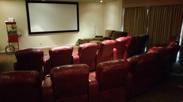 Una sala de cine en casa con sillones reclinables de cuero rojo, una pantalla grande y un proyector.