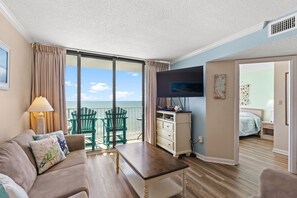 A room with a sofa, a coffee table, a TV, a dresser, and a view of the ocean. - Sands Beach Club II 917 Oceanfront Condo Close to Ocean Annie's (Myrtle Beach)