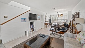 A modern living room with a sofa, coffee table, and a TV. There is a staircase leading to another room. - Sea Gate Villas 20 2 Bedroom Condo with Outdoor Pool! (Myrtle Beach)
