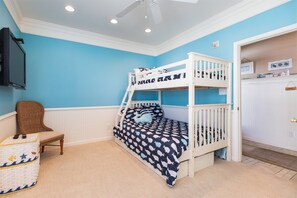 A bunk bed with a patterned bedspread, a television mounted on the wall, a wicker chair, and a small table with a basket.