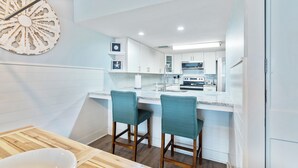 Una cocina moderna con armarios blancos, una isla central con taburetes de bar y un elemento decorativo en la pared.