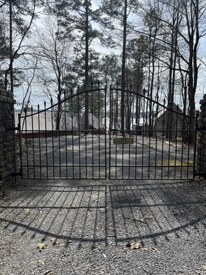 A gated driveway leading to a building with a metal roof, surrounded by trees and a clear sky. - Dock. Waterslide. Beach. Firepit, Gazebo, 500ft water frontage. Views. Sleep 18. (Equality)