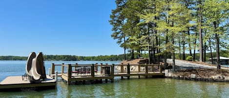 Eine Holzstele, die sich in einen See erstreckt, mit blauem Himmel, umgeben von Bäumen.