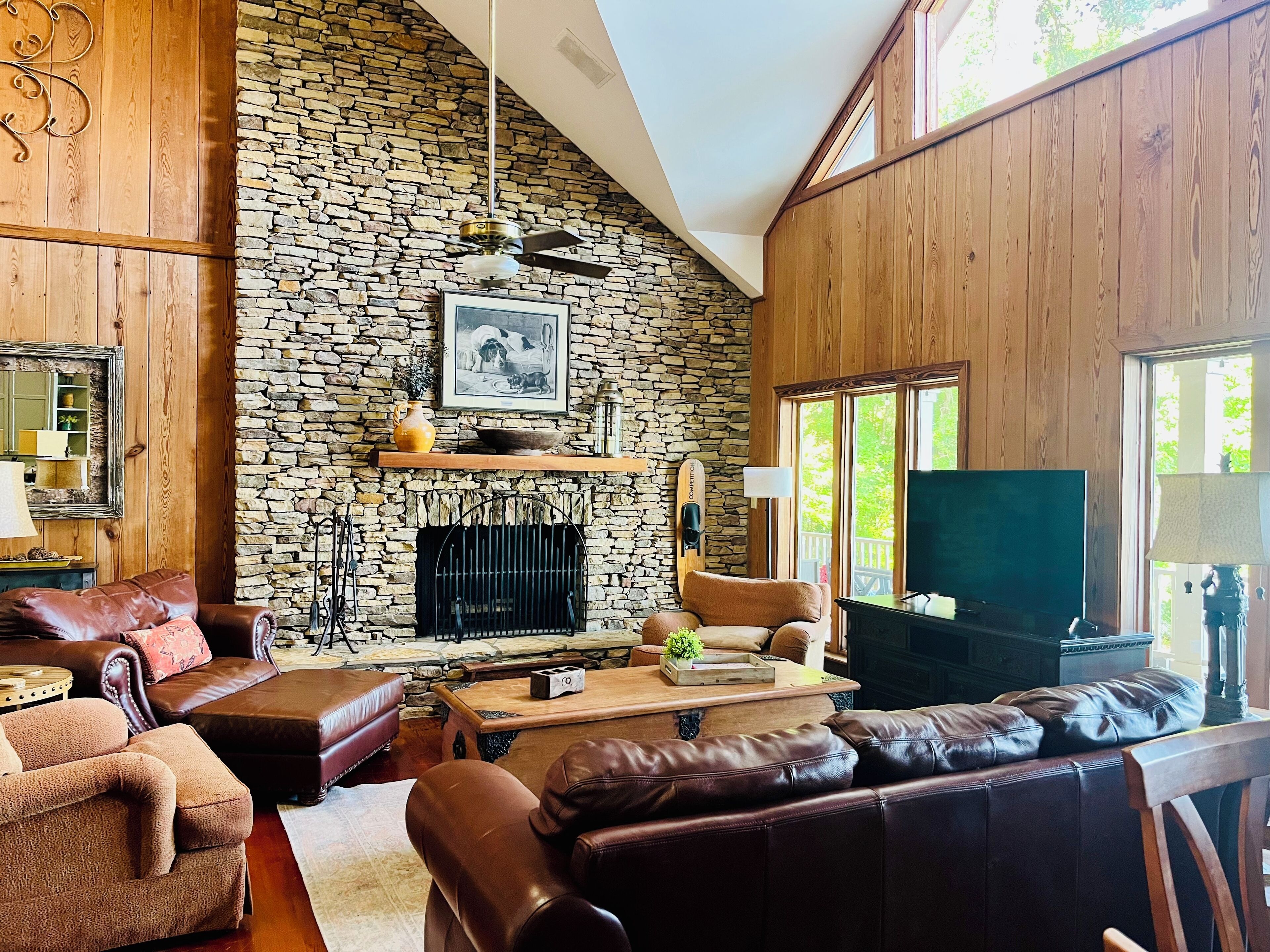A cozy living room with a stone fireplace, leather sofas, a television, and a stone wall.
