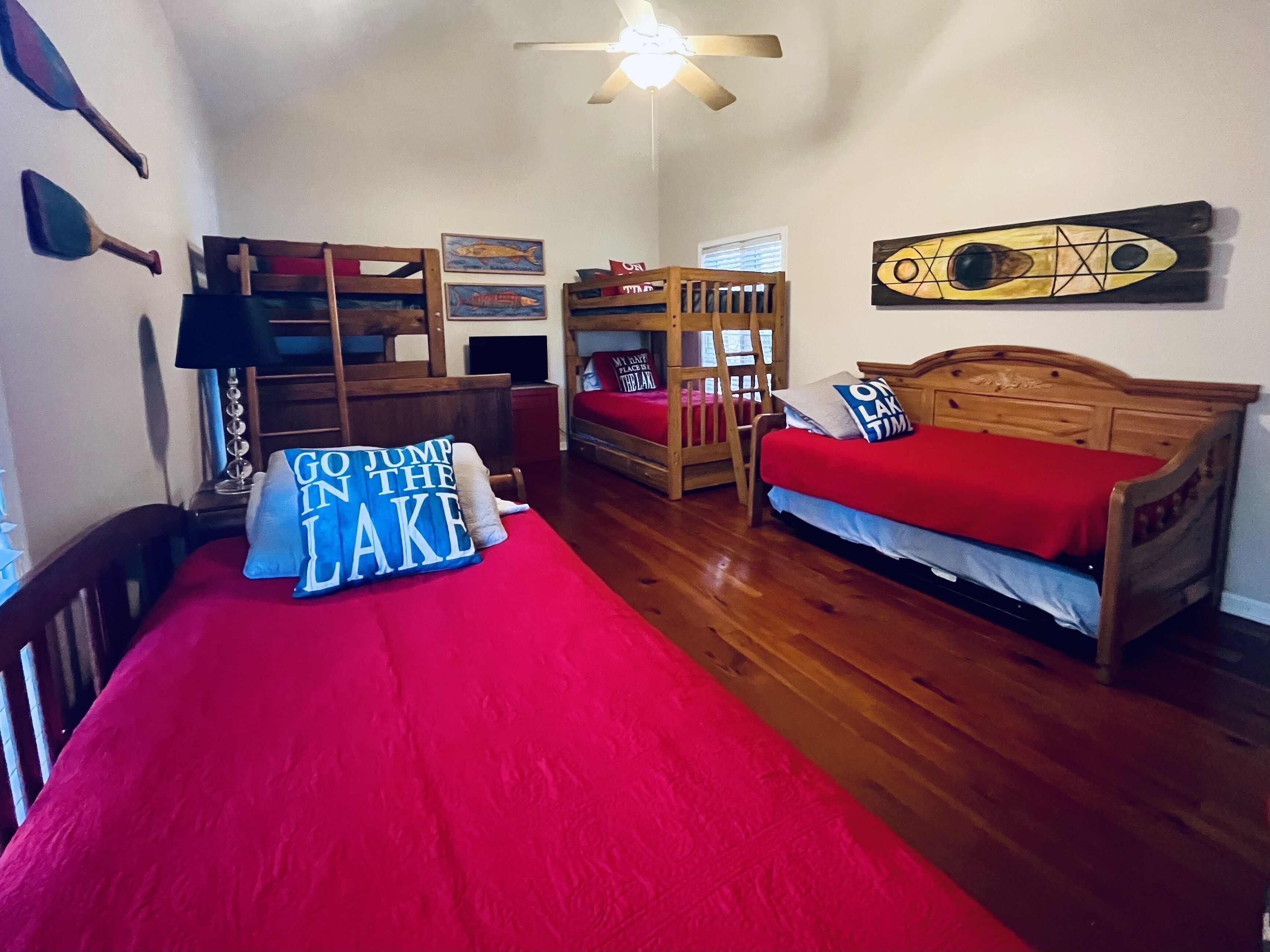 A room with two bunk beds, a wooden desk, a chair, and a bed with a red blanket.