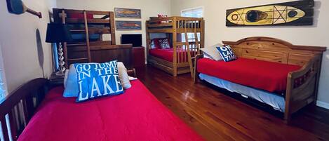 A room with two bunk beds, a wooden desk, a chair, and a bed with a red blanket.
