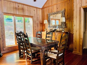 A wooden-paneled dining room with a glass table and chairs, a decorative mirror, and a view of the outdoors. - Dock. Waterslide. Beach. Firepit, Gazebo, 500ft water frontage. Views. Sleep 18. (Equality)