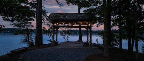 A gazebo with a gravel path leading to it, surrounded by trees and overlooking a body of water.