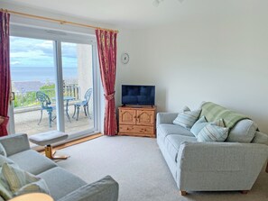 A living room with a sofa, a TV on a wooden cabinet, and a sliding glass door leading to an outdoor area with chairs and a table. - 2 bedroom accommodation in Cullen, near Buckie (Cullen, near Buckie)