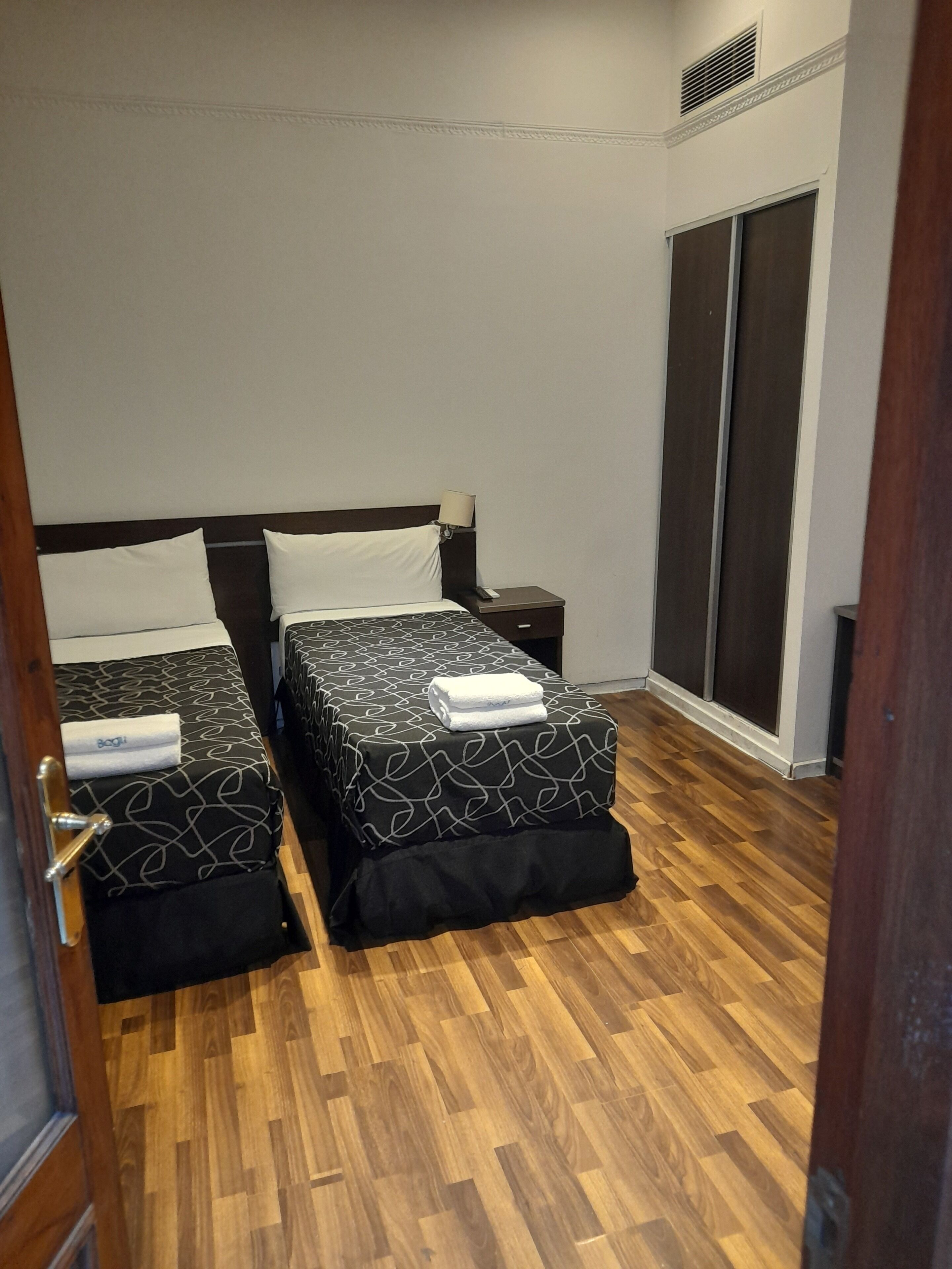Hotellihuone, jossa on kaksi sänkyä, vaatekaappi ja puulattia.