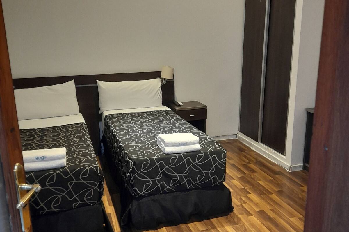 Una habitación de hotel con dos camas, un armario y suelo de madera.
