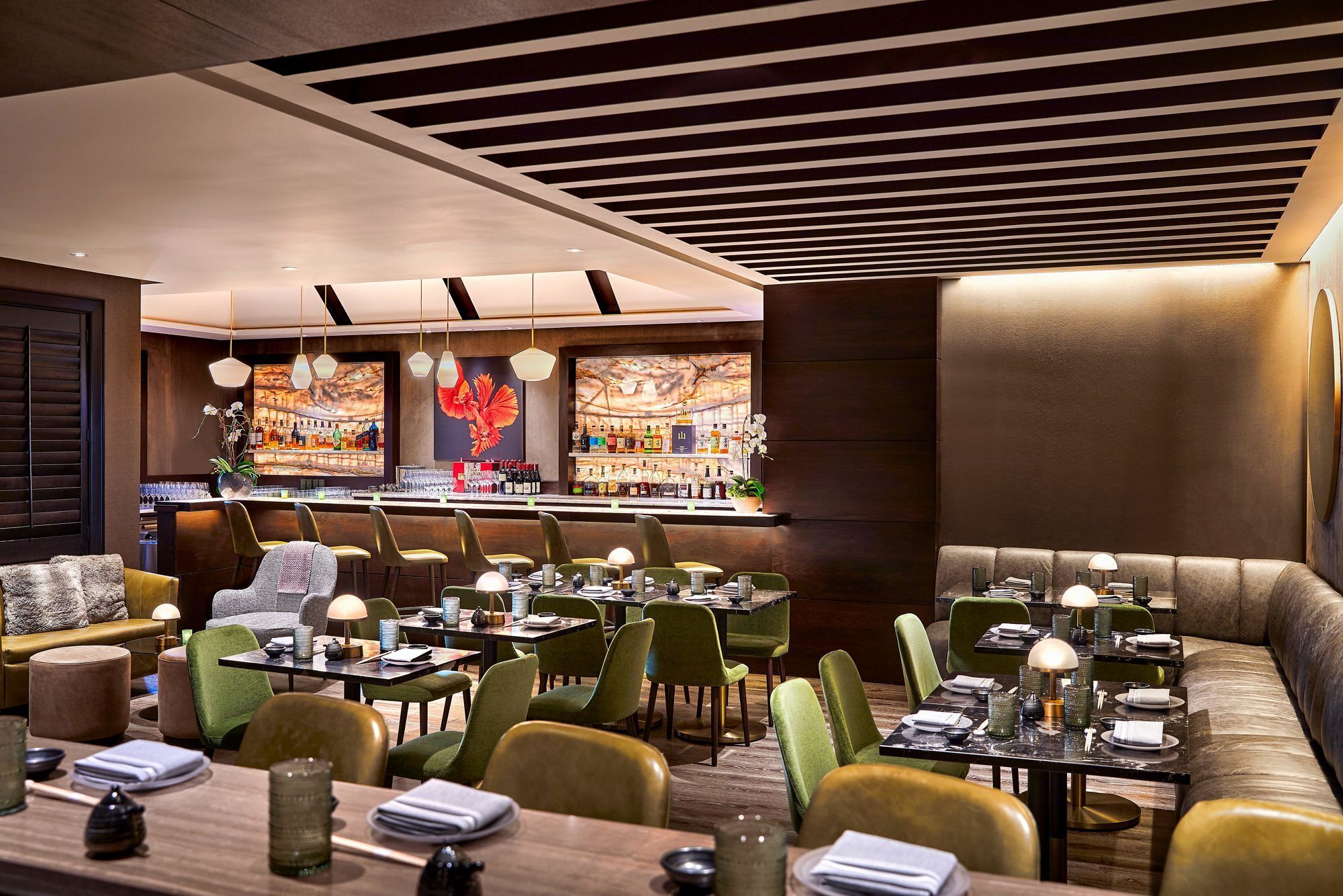A modern restaurant with a bar area, green upholstered chairs, and a cozy seating area with a sofa and armchairs.