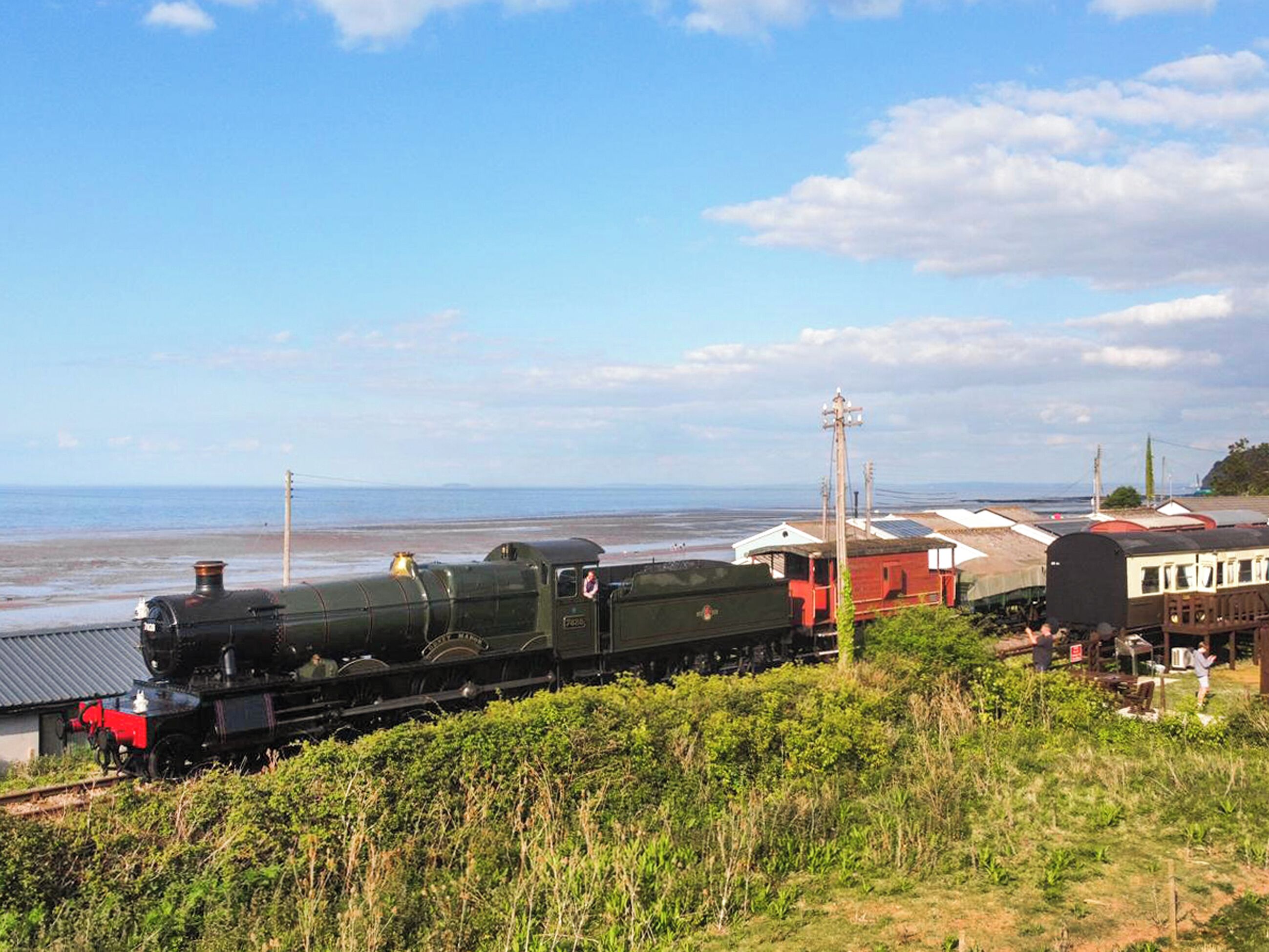 Une locomotive à vapeur sur des rails, avec une plage et l’océan en arrière-plan.